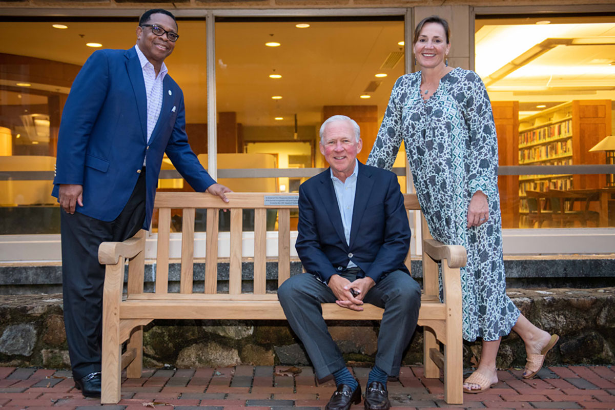 David Routh seated on a bench with Jesse Cureton standing behind the bench to his right and Jane Ellison leaning on the bench to his left