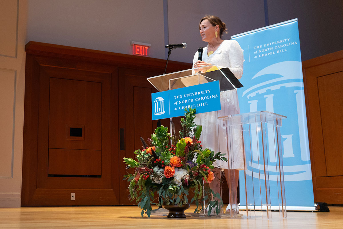 Ellison stands on a stage behind a podium with a bouquet in the foreground