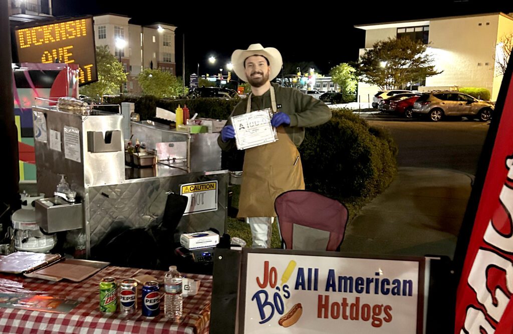 Joe Spencer holds a certificate for a perfect sanitation rating beside his hot dog stand.