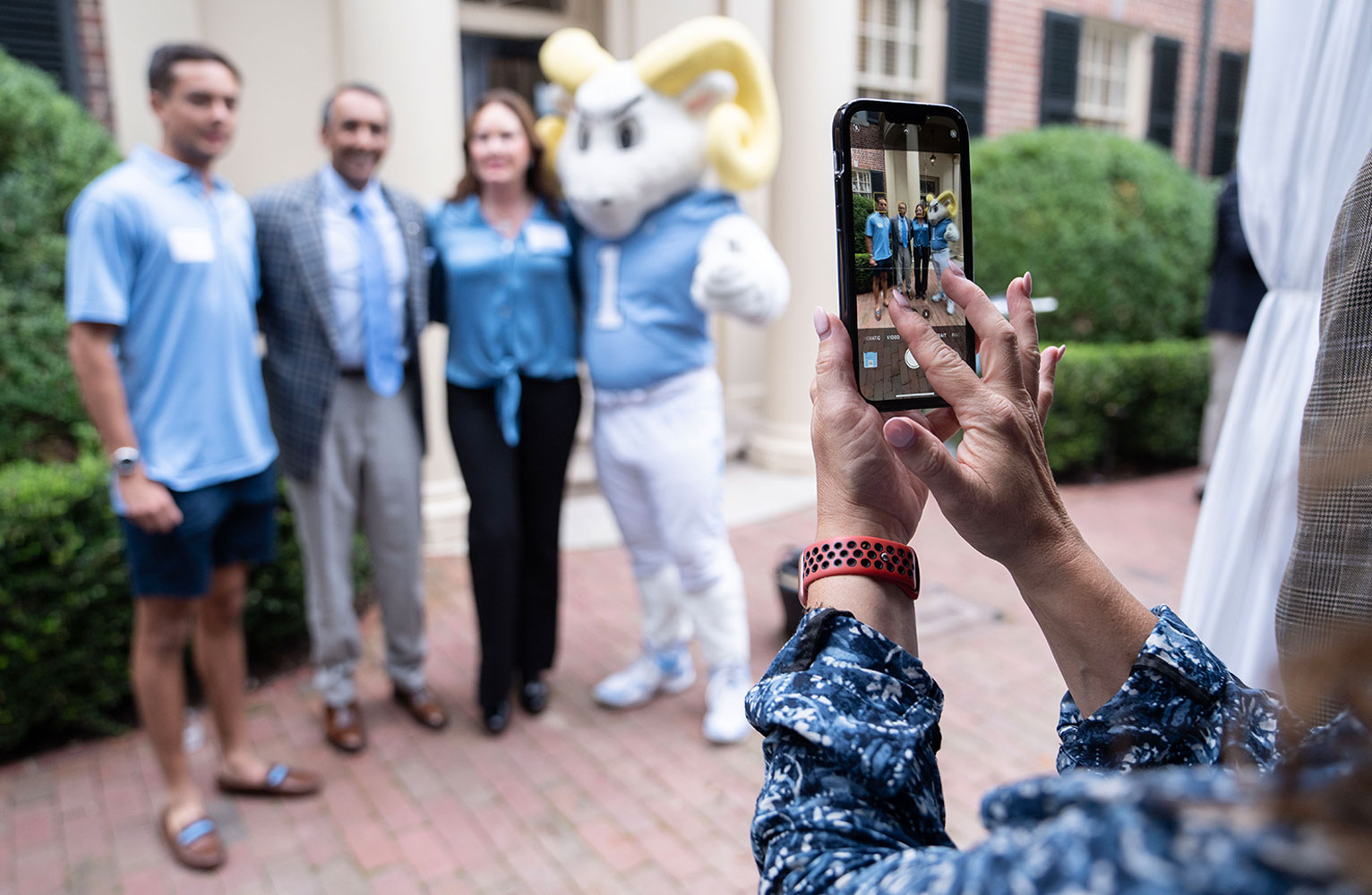 A woman's hands zoom in on a smartphone taking picture of a family standing in front of the Carolina Inn