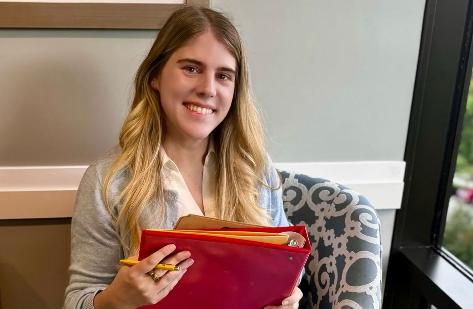 Sarah McGlothlin smiles at the camera holding a red binder