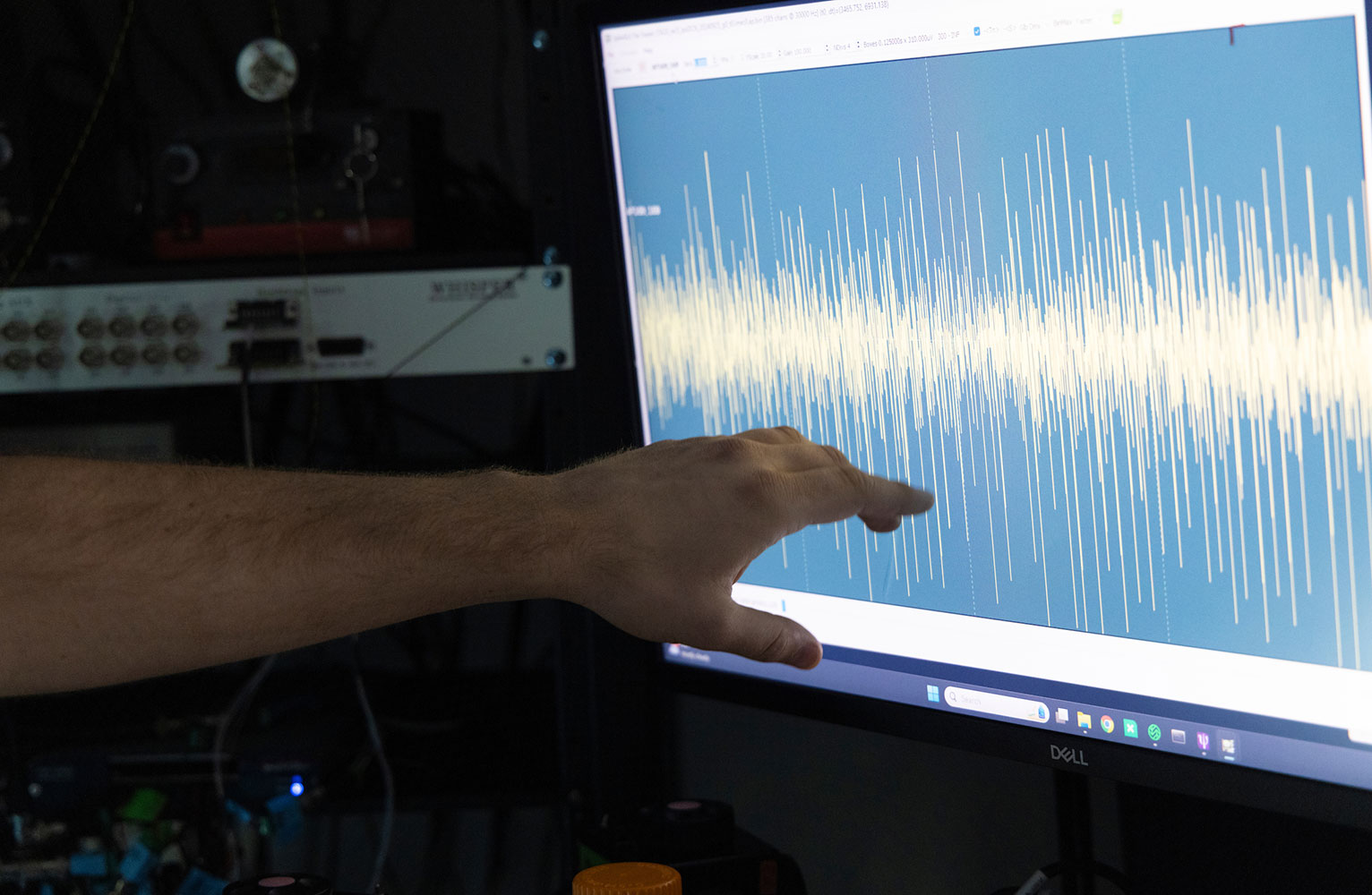 A hand points out brain waves displayed on a computer monitor