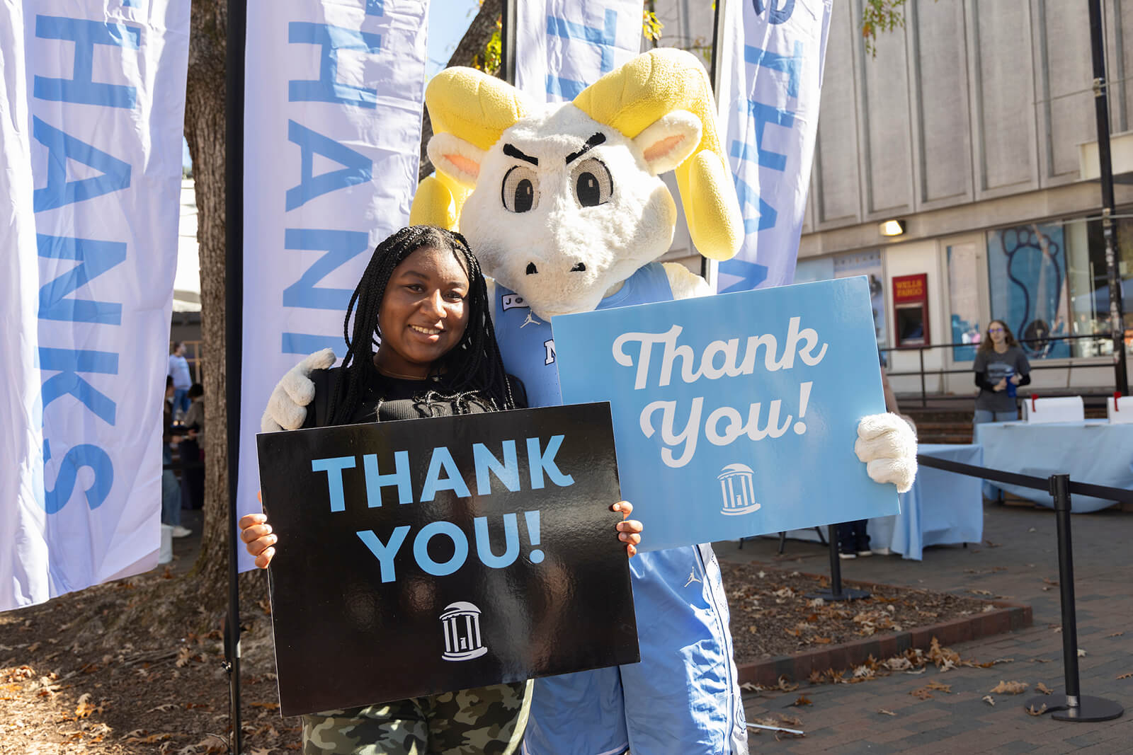 A Carolina student and mascot Rameses holding up signs thanking donors