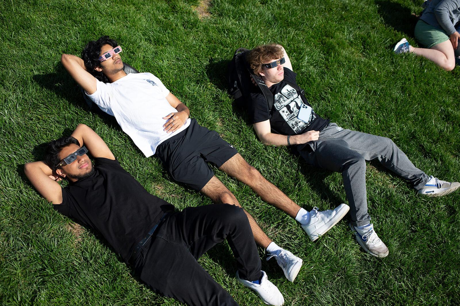 Carolina students lying on grass while wearing eclipse glasses