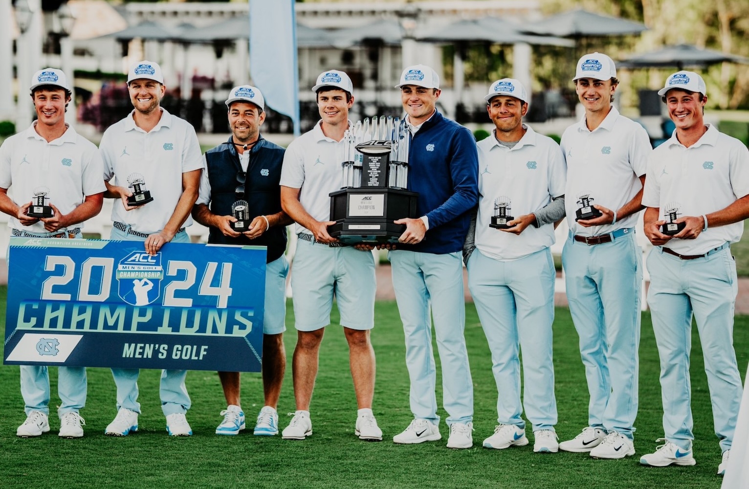 The 2024 UNC mens golf team holding trophies and a banner after winning the ACC championship.