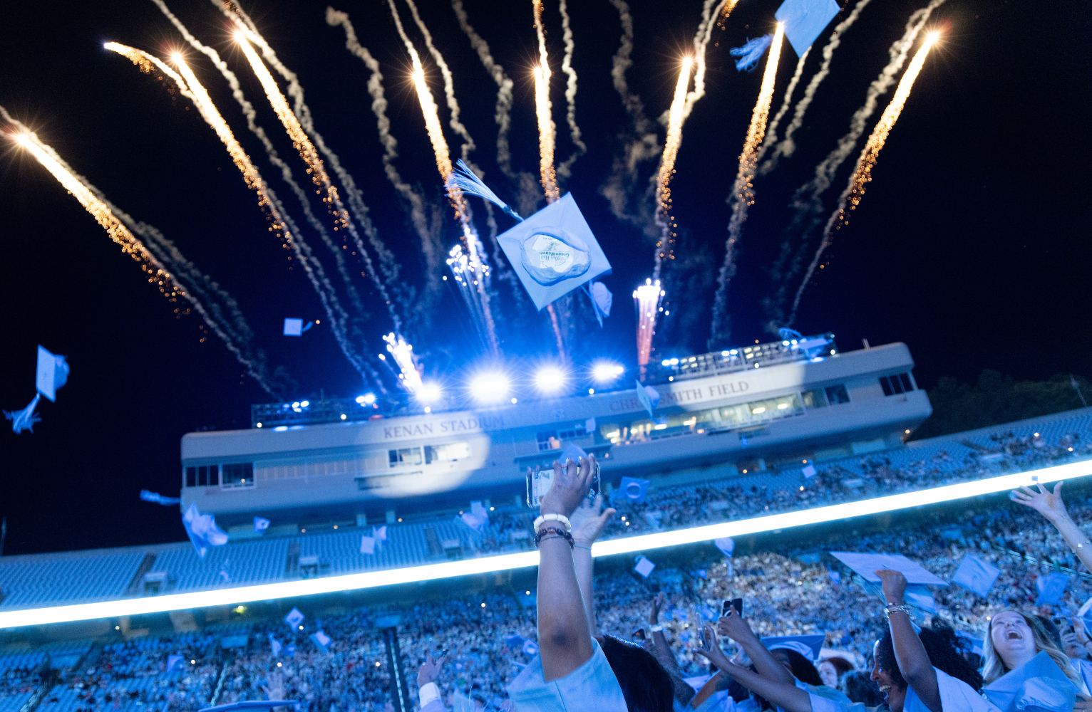 Graduation caps flying in the air as fireworks shoot off the top of Kenan Stadium.