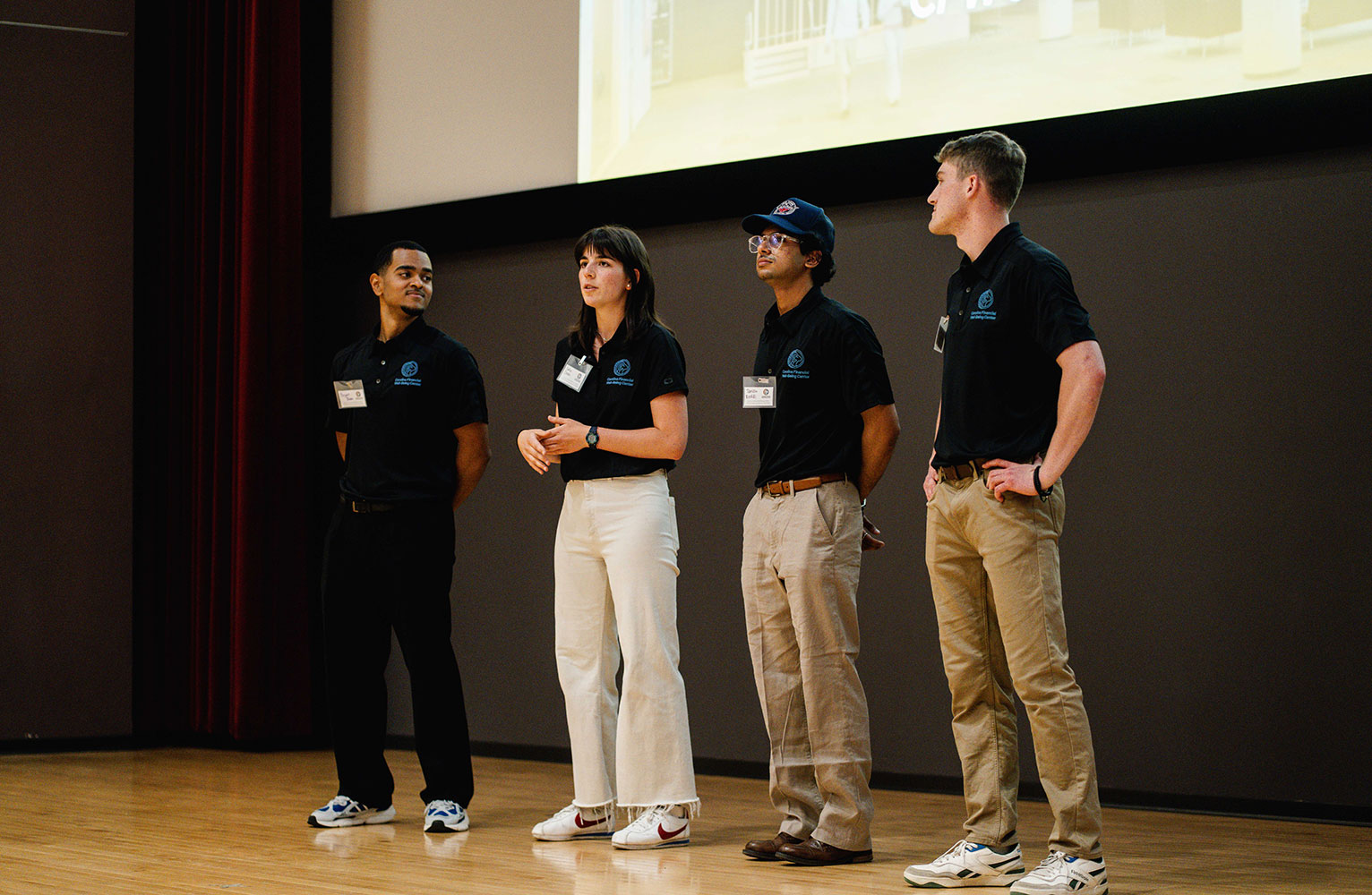 Four student coaches and peers stand on a stage