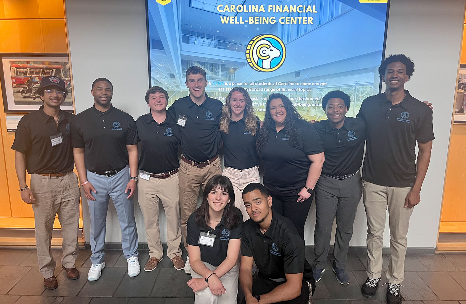 A group of Carolina students pose for a portrait in front of a screen with the words Carolina Financial Well-Being Center written on it