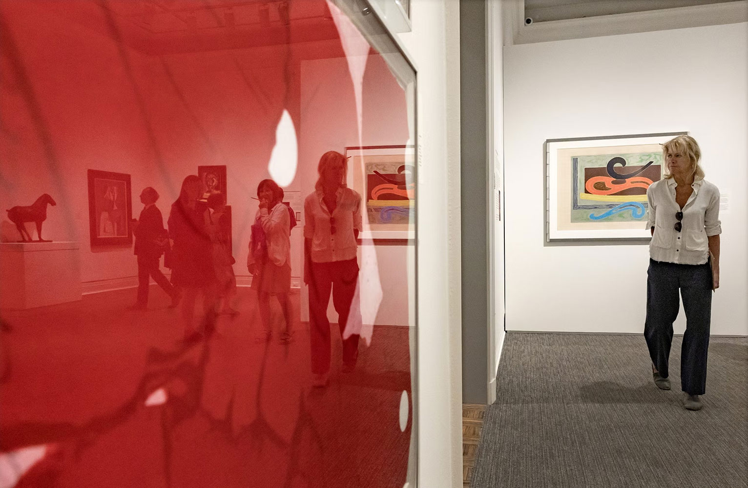 An artwork featuring the color red in the foreground with a woman viewing other artworks in the "Color Triumphant" exhibit in the background
