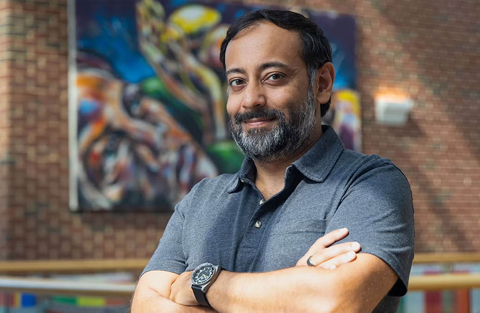 Nabarun Dasgupta stands smiling with arms crossed with a colorful artwork in the background.