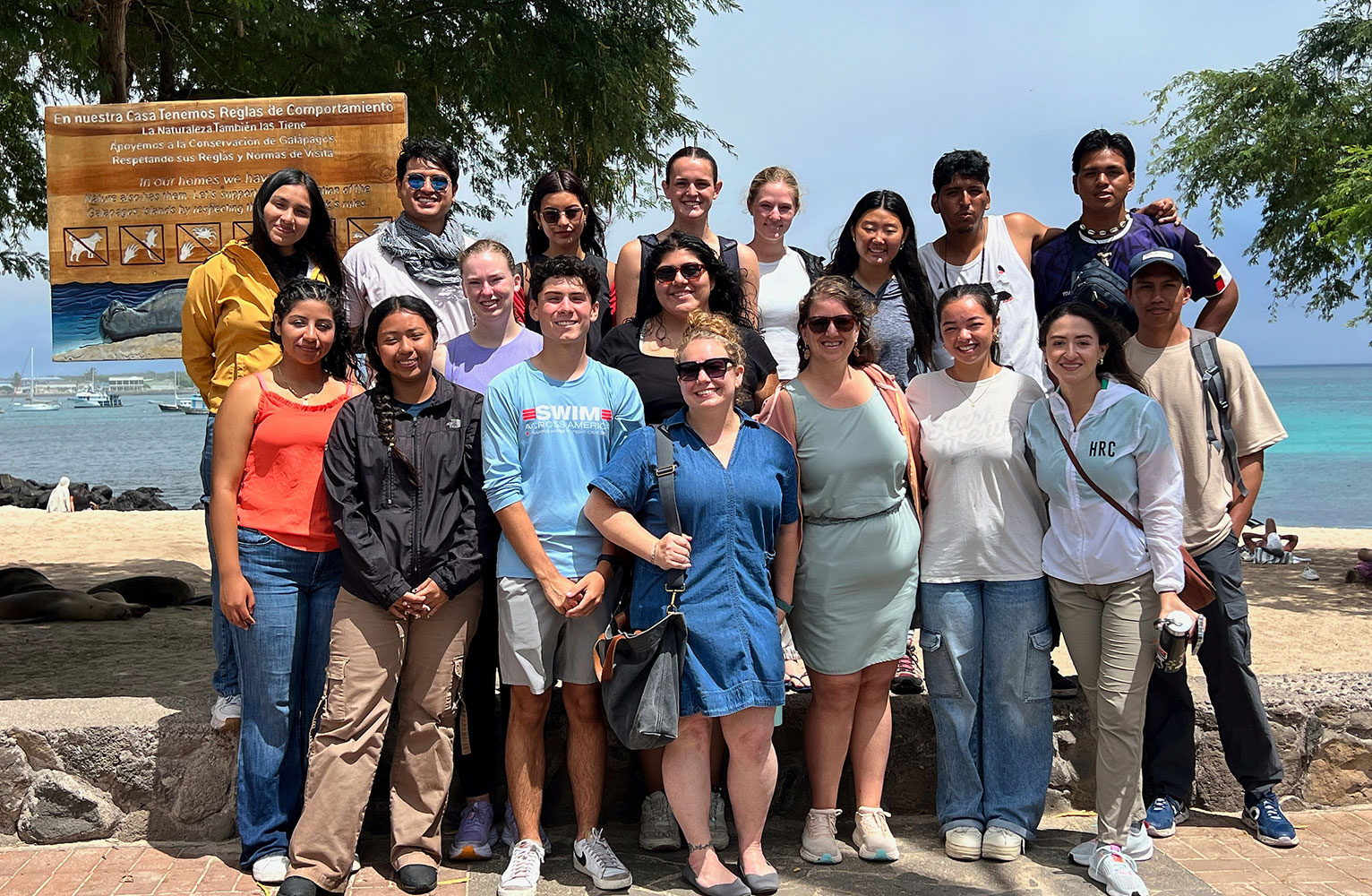 A large group of students and faculty pose for the camera withe the ocean in the background.