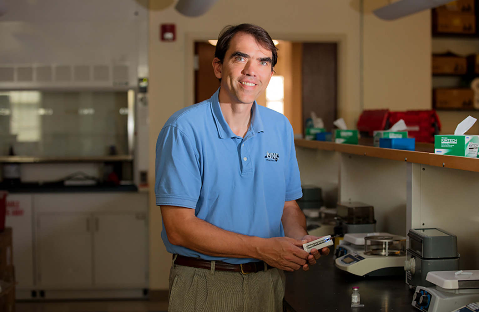 Stephen Eckel poses in his lab holding his IV dosing device