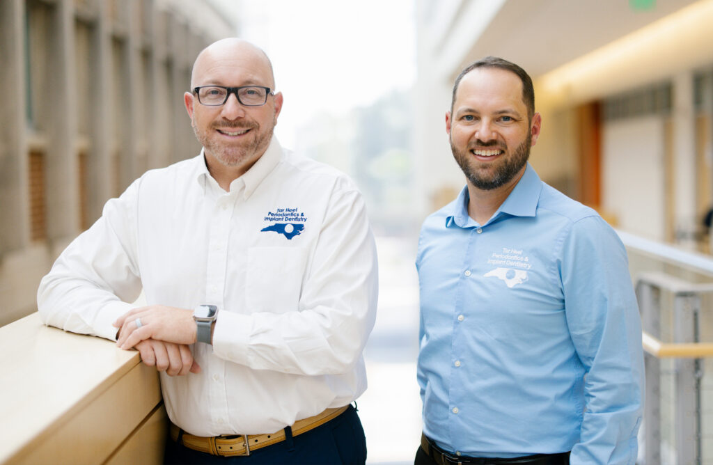 Two men smile and pose for the camera in a brightly lit atrium.