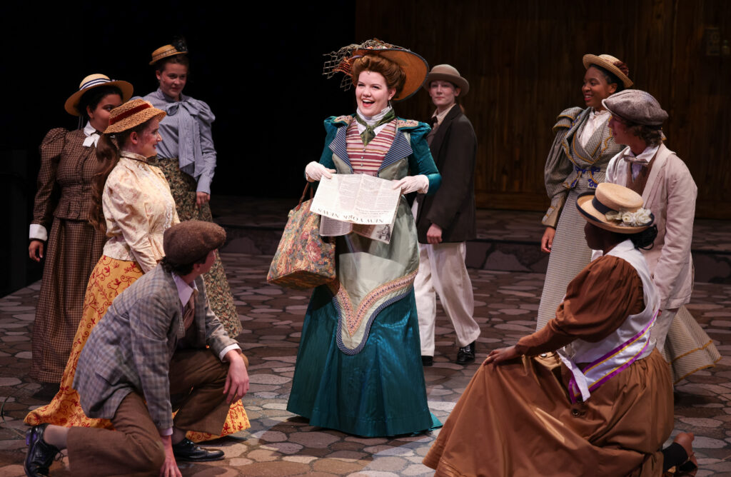 Actors performing a musical on stage wearing 19th century attire.
